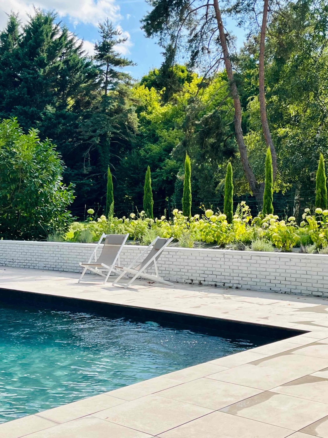 Het verwarmde zwembad, met ligstoelen en bloeiende tuin